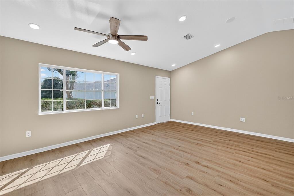 An empty room features light wood-look flooring, beige walls, a ceiling fan, and a window — 13520 SE 87TH CIRCLE, SUMMERFIELD, FL