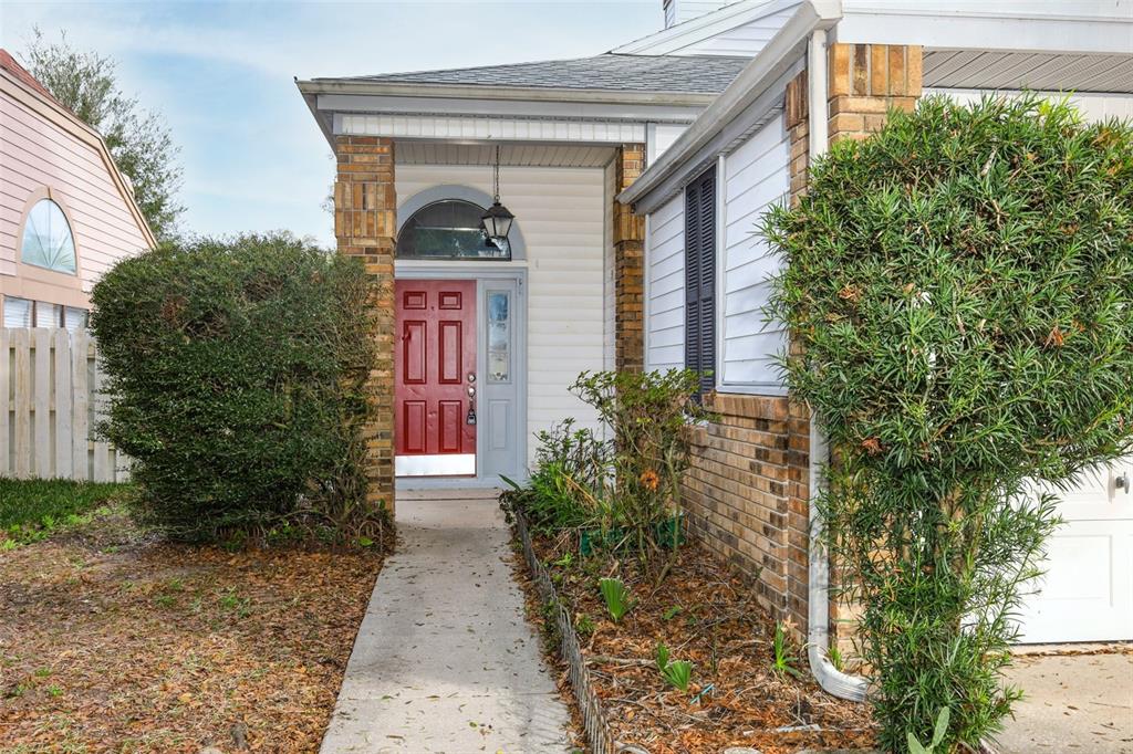 A red front door with a sidelight and arched transom sits under a covered porch — 5405 RUTLAND COURT, ORLANDO, FL