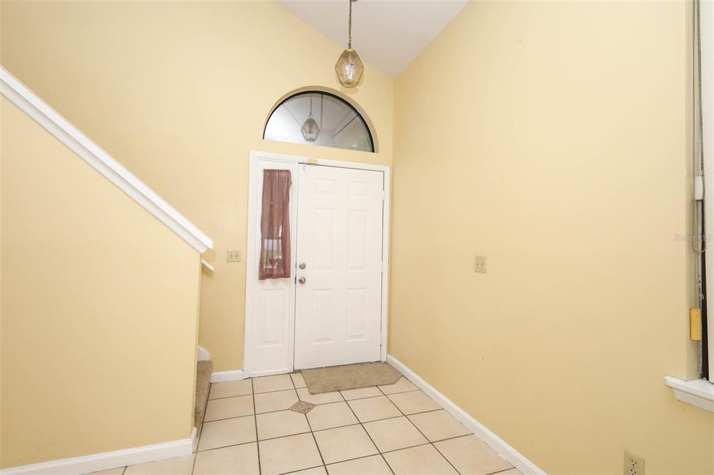 An entryway features a white front door with a sidelight, tiled flooring, and yellow walls — 5405 RUTLAND COURT, ORLANDO, FL