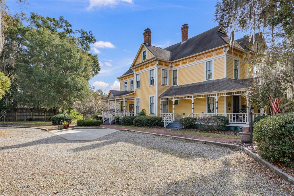 A yellow two-story Victorian house with a wrap-around porch sits beside a gravel driveway — 221 SE 7TH STREET, GAINESVILLE, FL