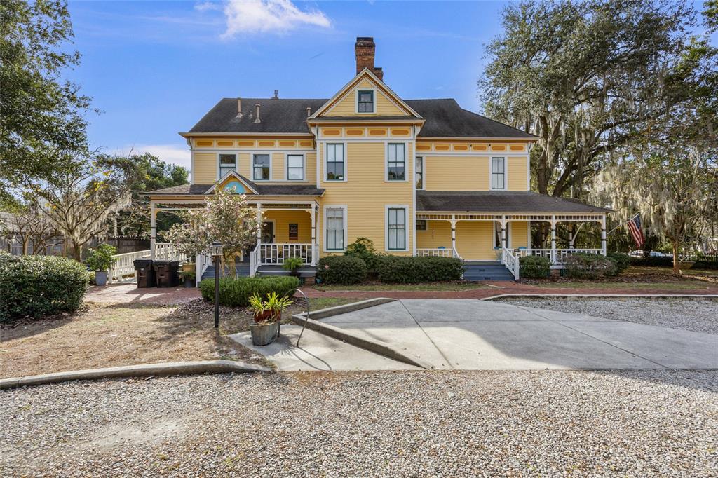 A yellow two-story historic house features a wrap-around porch and a gravel driveway — 221 SE 7TH STREET, GAINESVILLE, FL