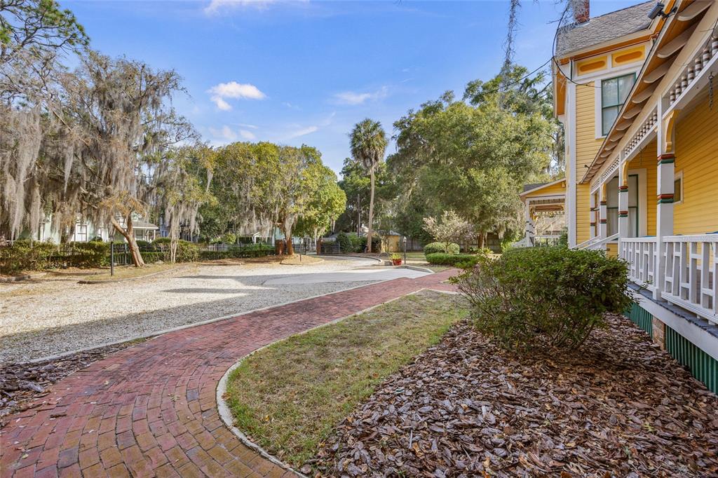 A brick walkway leads toward a yellow house with a white porch and gravel driveway — 221 SE 7TH STREET, GAINESVILLE, FL