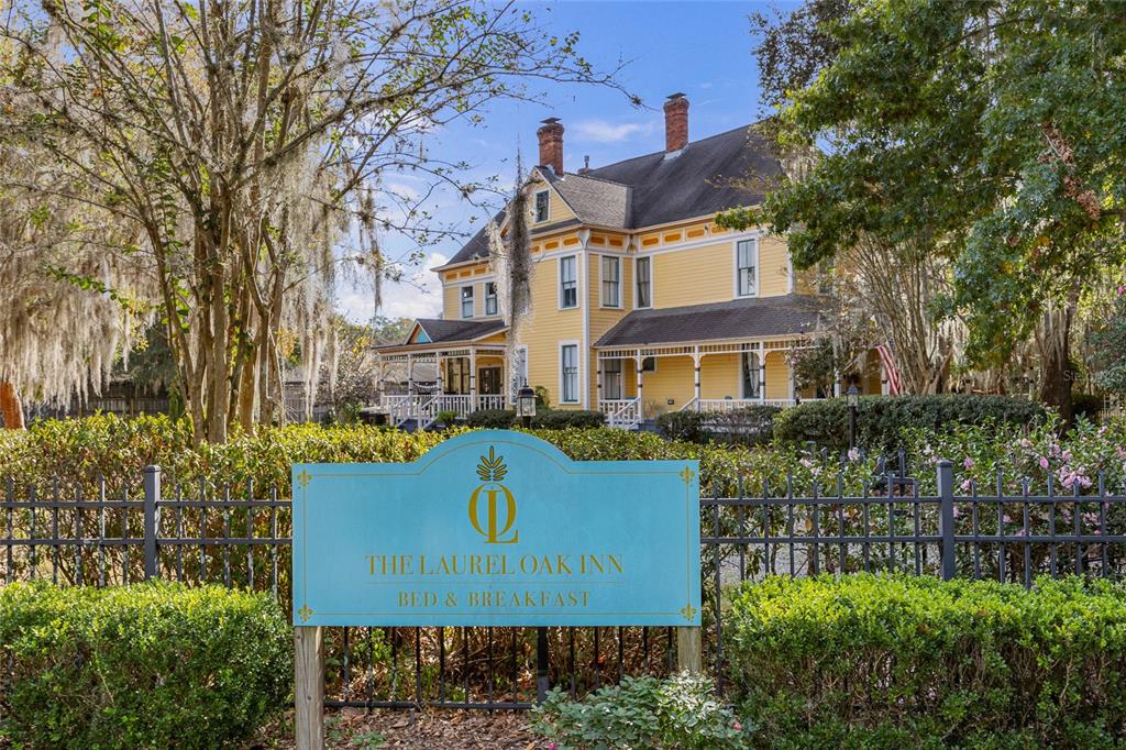 A yellow historic house stands behind a blue sign for The Laurel Oak Inn — 221 SE 7TH STREET, GAINESVILLE, FL