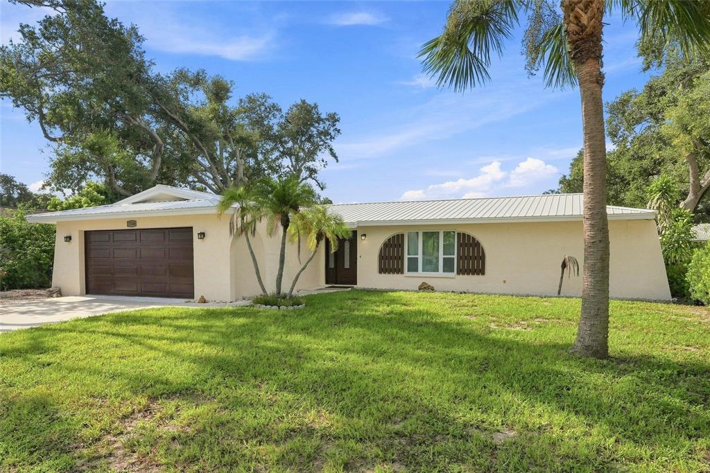 A single-story house with a metal roof, beige stucco exterior, and a two-car garage — 13344 88TH AVENUE, SEMINOLE, FL