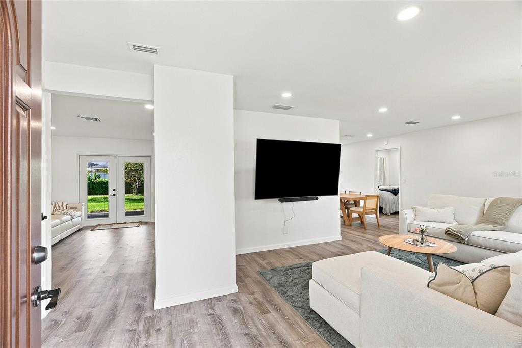 A bright living room features white walls, wood-look flooring, a wall-mounted television, and neutral furniture — 13344 88TH AVENUE, SEMINOLE, FL