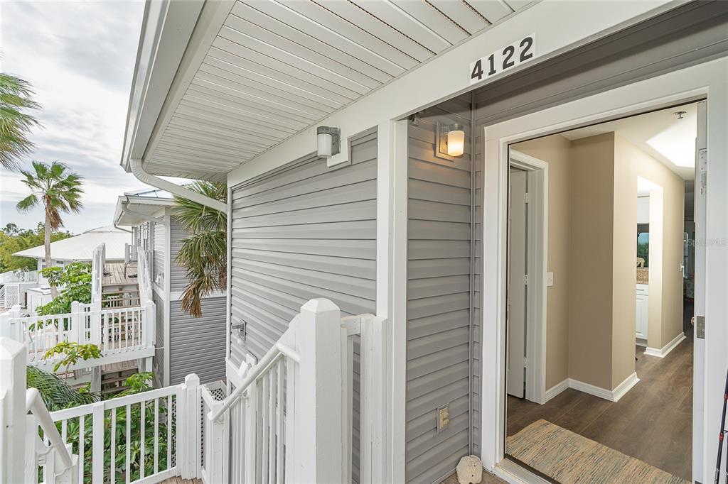 An exterior view of a house entrance with gray siding, white railings, and a wooden deck — 7201 RUM BAY DR UNIT 4122A, PLACIDA, FL