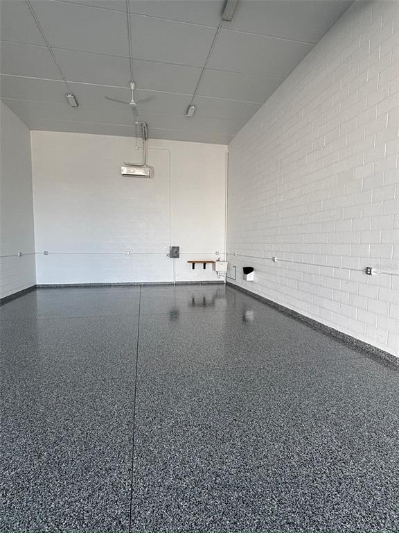 A spacious garage with white brick walls, a gray epoxy floor, and a ceiling fan — 5225 TAYLOR ROAD UNIT A9, PUNTA GORDA, FL