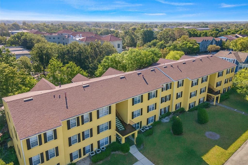 An aerial view of a three-story yellow apartment building with a brown shingled roof — 2059 DIXIE BELLE DR UNIT 2059n, ORLANDO, FL