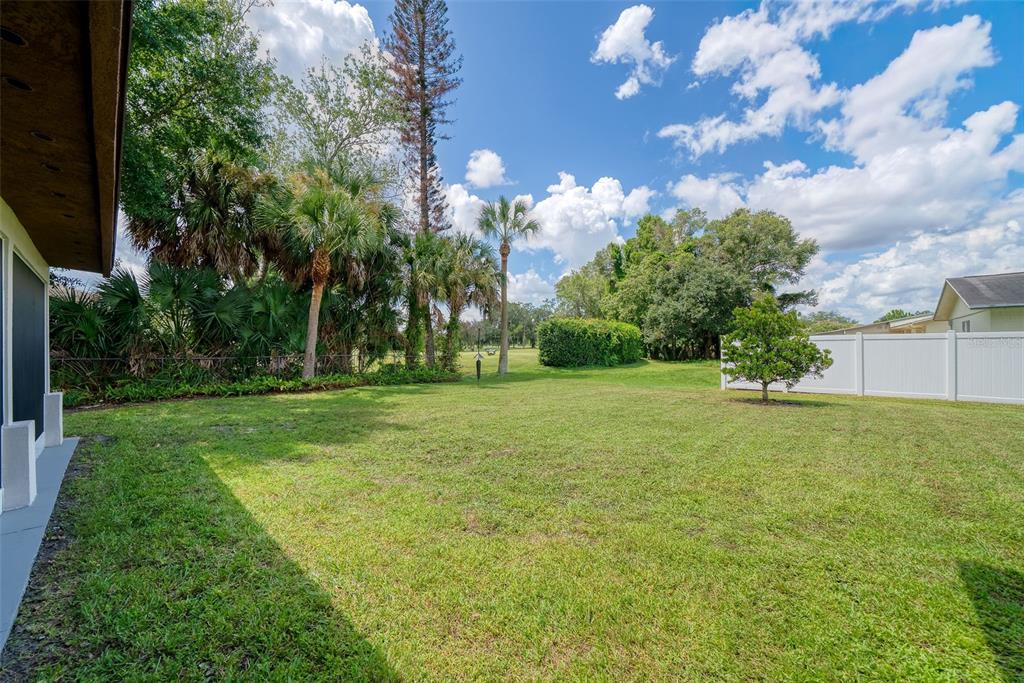 A grassy backyard features a white fence, palm trees, and a view of a golf course — 943 FAIRWAY DRIVE, WINTER PARK, FL