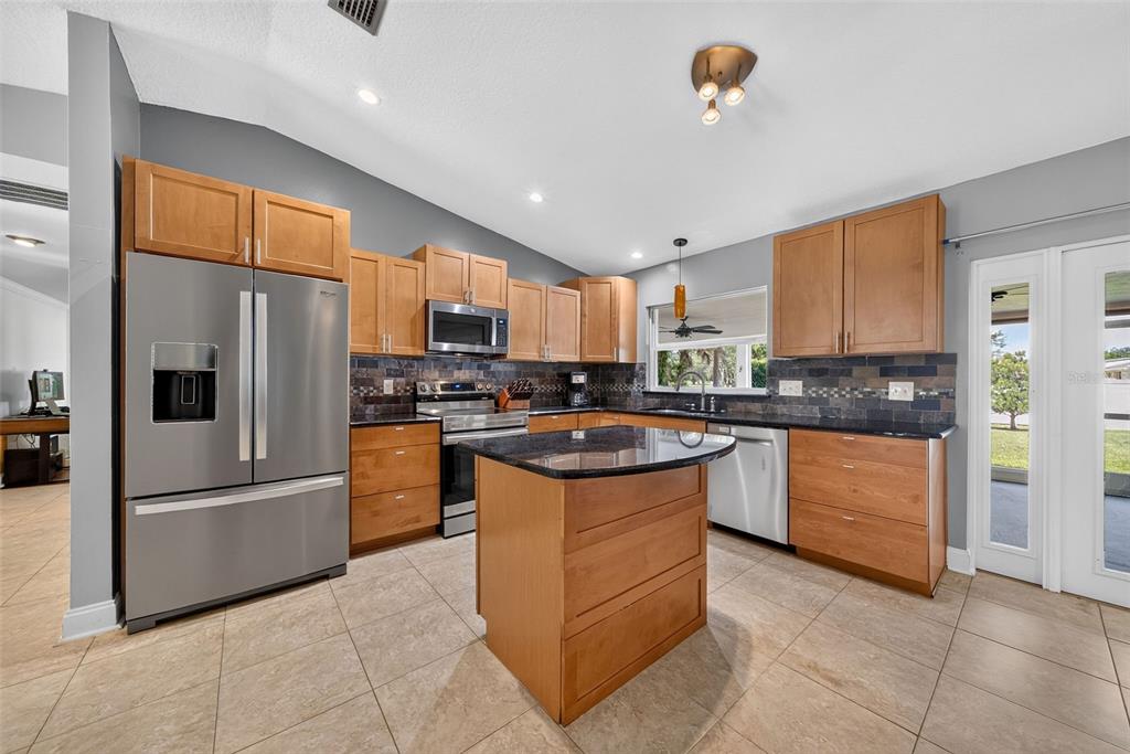 A kitchen features wood cabinets, stainless steel appliances, a center island, and dark tile backsplash — 943 FAIRWAY DRIVE, WINTER PARK, FL