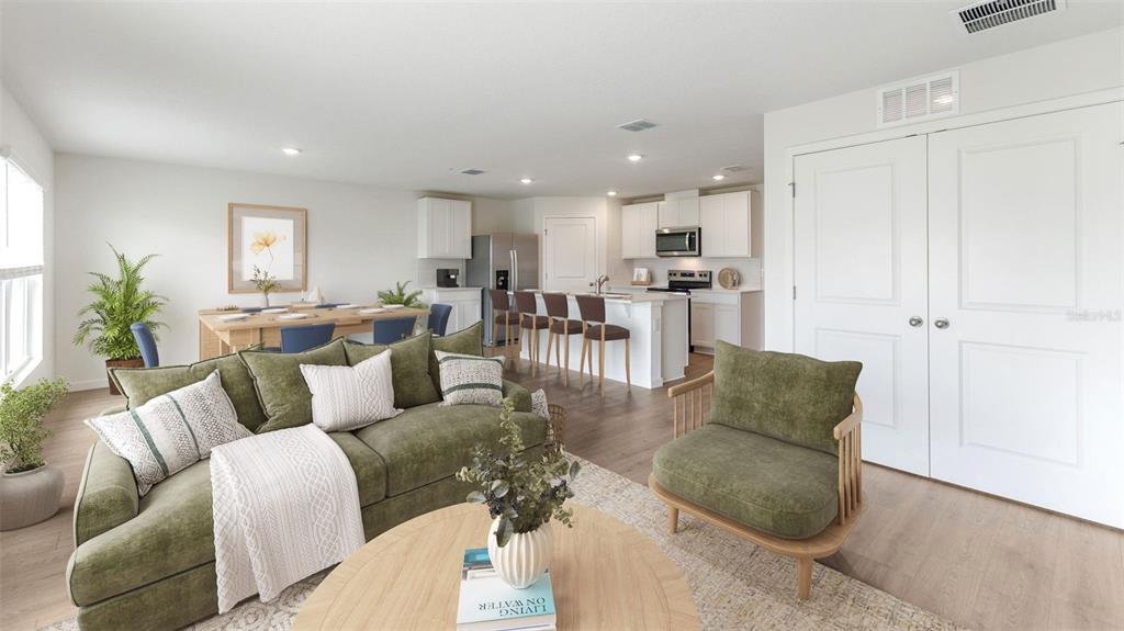 An open-concept living room and kitchen feature a green sofa, dining area, and island seating — 3080 PIGEON COVE STREET, DELTONA, FL