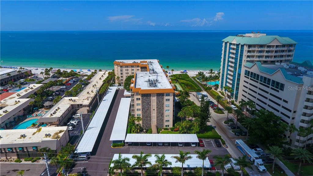 An aerial view shows a multi-story apartment building near a beach with covered parking areas — 800 BENJAMIN FRANKLIN DRIVE UNIT 403, SARASOTA, FL