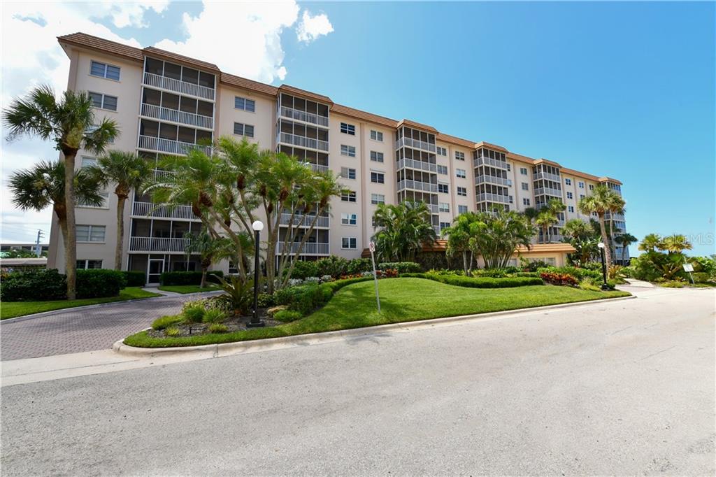 A multi-story apartment building with screened balconies stands behind a landscaped lawn and palm trees — 800 BENJAMIN FRANKLIN DRIVE UNIT 403, SARASOTA, FL