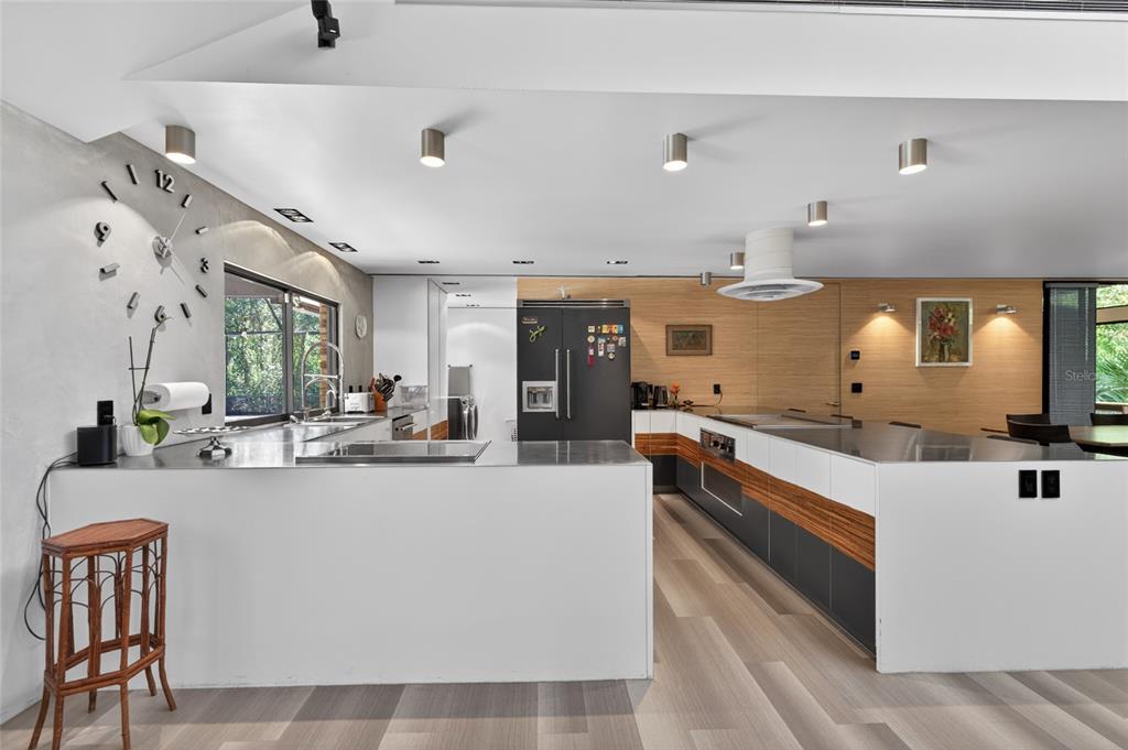 A modern kitchen features stainless steel countertops, dark cabinetry, and a large wall-mounted clock — 5425 SADDLEBROOK WAY, WESLEY CHAPEL, FL