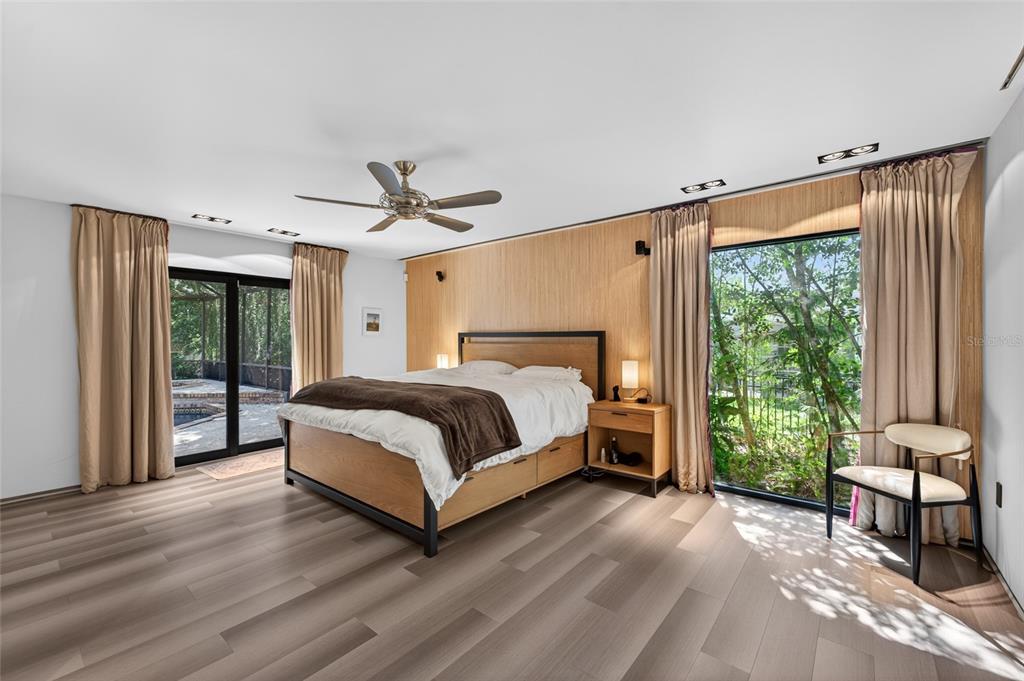 A bedroom features wood-paneled walls, a platform bed, light wood flooring, and large glass doors — 5425 SADDLEBROOK WAY, WESLEY CHAPEL, FL