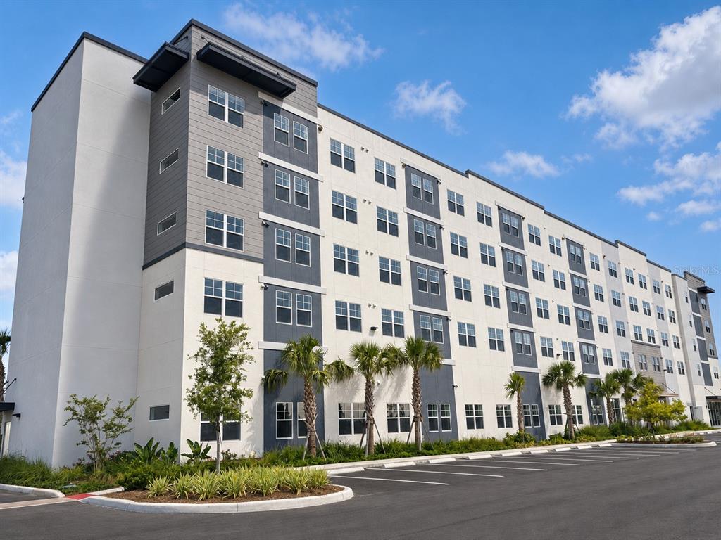 A multi-story apartment building with a gray and white exterior stands beside a parking lot — 5563 MILLENIA PARK BOULEVARD UNIT 322, ORLANDO, FL