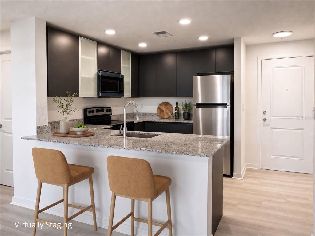 A kitchen with dark cabinets, granite countertops, stainless steel appliances, and two bar stools — 5563 MILLENIA PARK BOULEVARD UNIT 322, ORLANDO, FL