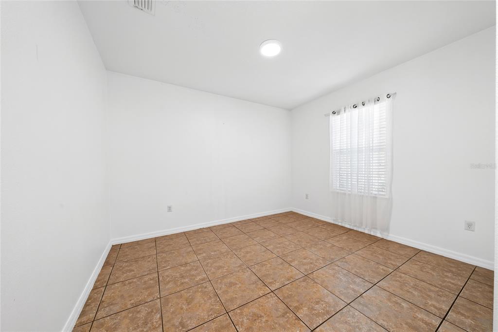 An empty room with white walls, a single window with curtains, and brown tiled flooring — 5590 SILVER THISTLE LANE, ST CLOUD, FL