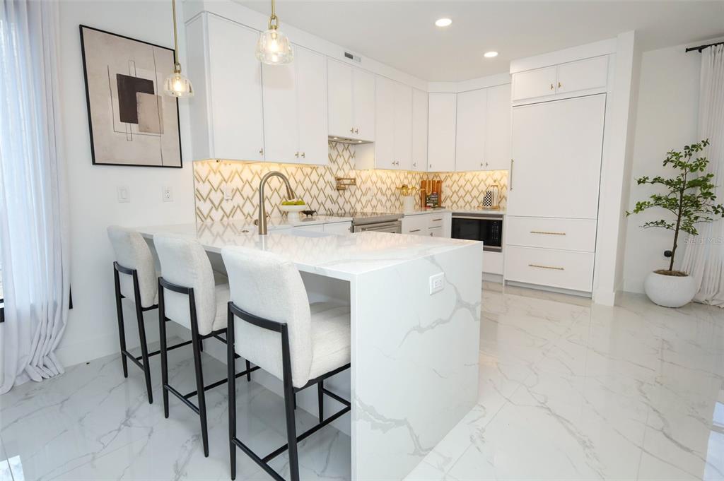 A modern kitchen features white cabinetry, a marble-topped island with bar stools, and patterned backsplash — 2360 OCEAN SHORE BOULEVARD UNIT 203, ORMOND BEACH, FL