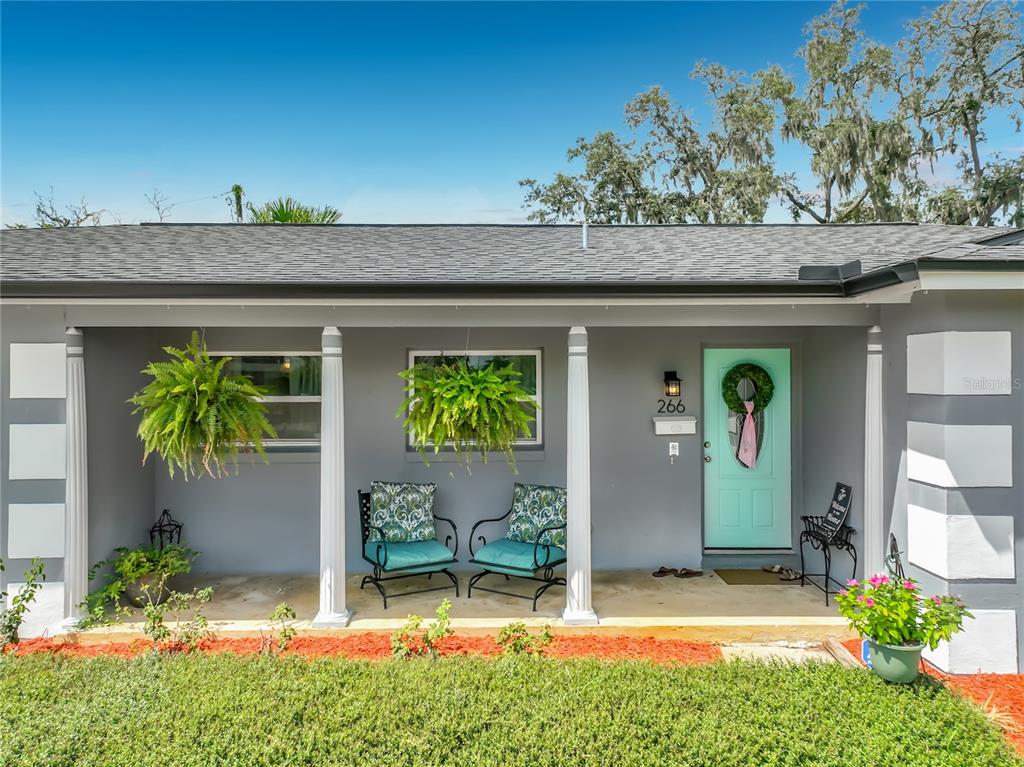 A gray house exterior features a covered porch with two chairs, hanging plants, and a door — 266 CARRIAGE HILL DRIVE, CASSELBERRY, FL