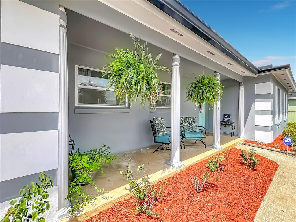 A covered front porch features gray walls, white columns, hanging ferns, and two chairs — 266 CARRIAGE HILL DRIVE, CASSELBERRY, FL