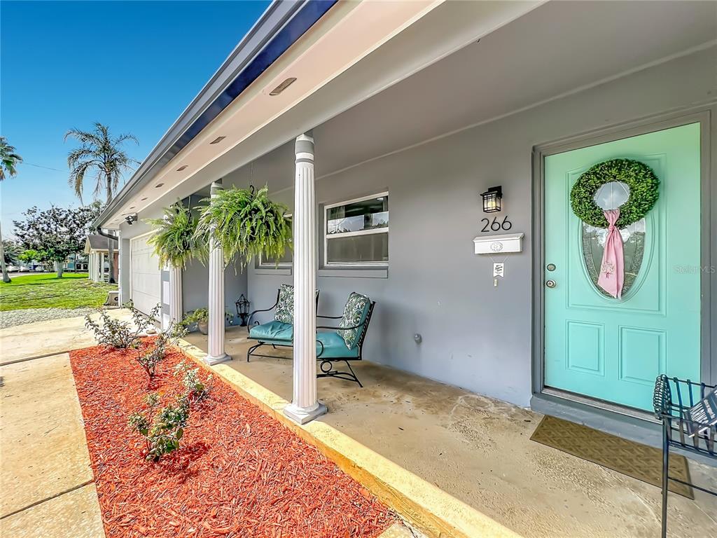 A covered porch features a light blue front door, two chairs, and hanging plants — 266 CARRIAGE HILL DRIVE, CASSELBERRY, FL