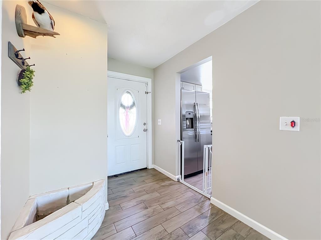 An entryway with wood-look tile flooring leads to a white front door and a kitchen — 266 CARRIAGE HILL DRIVE, CASSELBERRY, FL