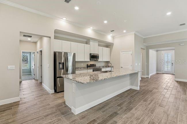A kitchen with white cabinets, granite countertops, a stainless steel refrigerator, and wood-look tile flooring — 11 SANDERS CIRCLE, HOMOSASSA, FL