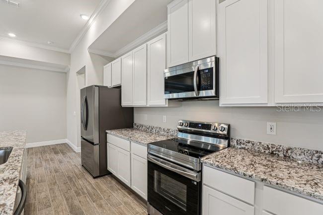 A kitchen features white cabinets, stainless steel appliances, and granite countertops over wood-look tile flooring — 11 SANDERS CIRCLE, HOMOSASSA, FL