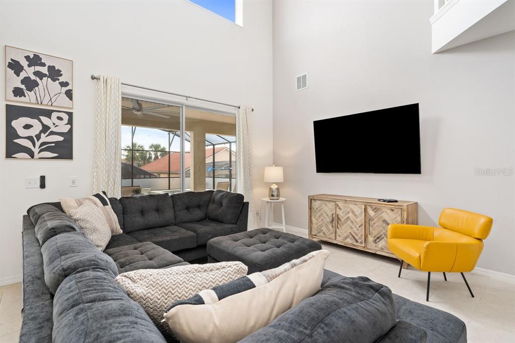 A living room features a large gray sectional sofa, a yellow armchair, and a wall-mounted television — 166 CARRERA AVENUE, DAVENPORT, FL