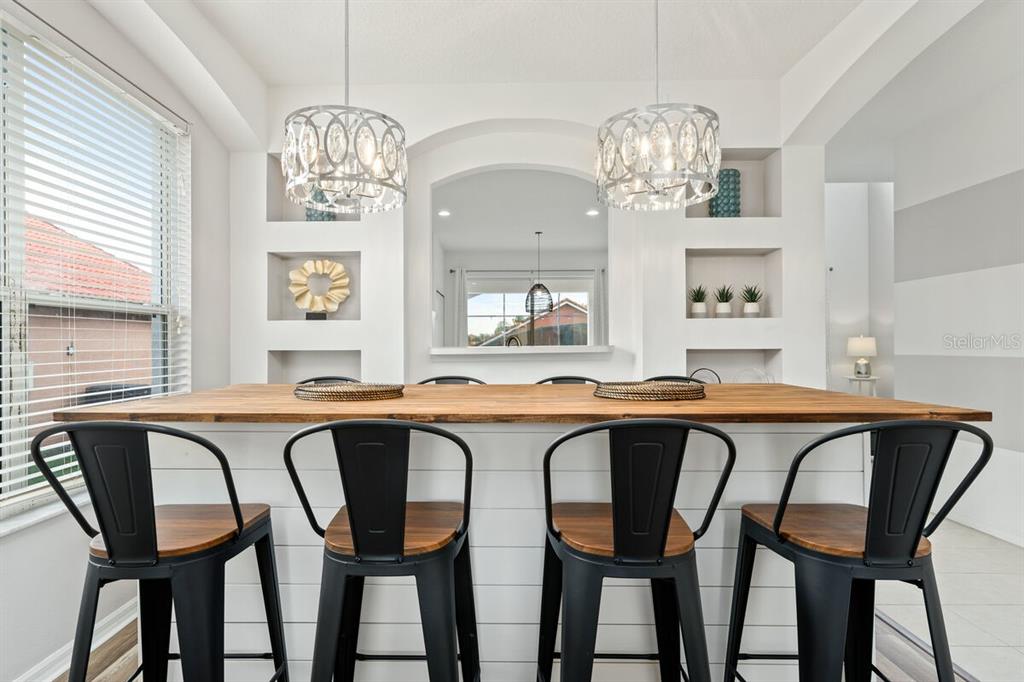 A kitchen island with four black metal stools sits in front of built-in wall shelving — 166 CARRERA AVENUE, DAVENPORT, FL