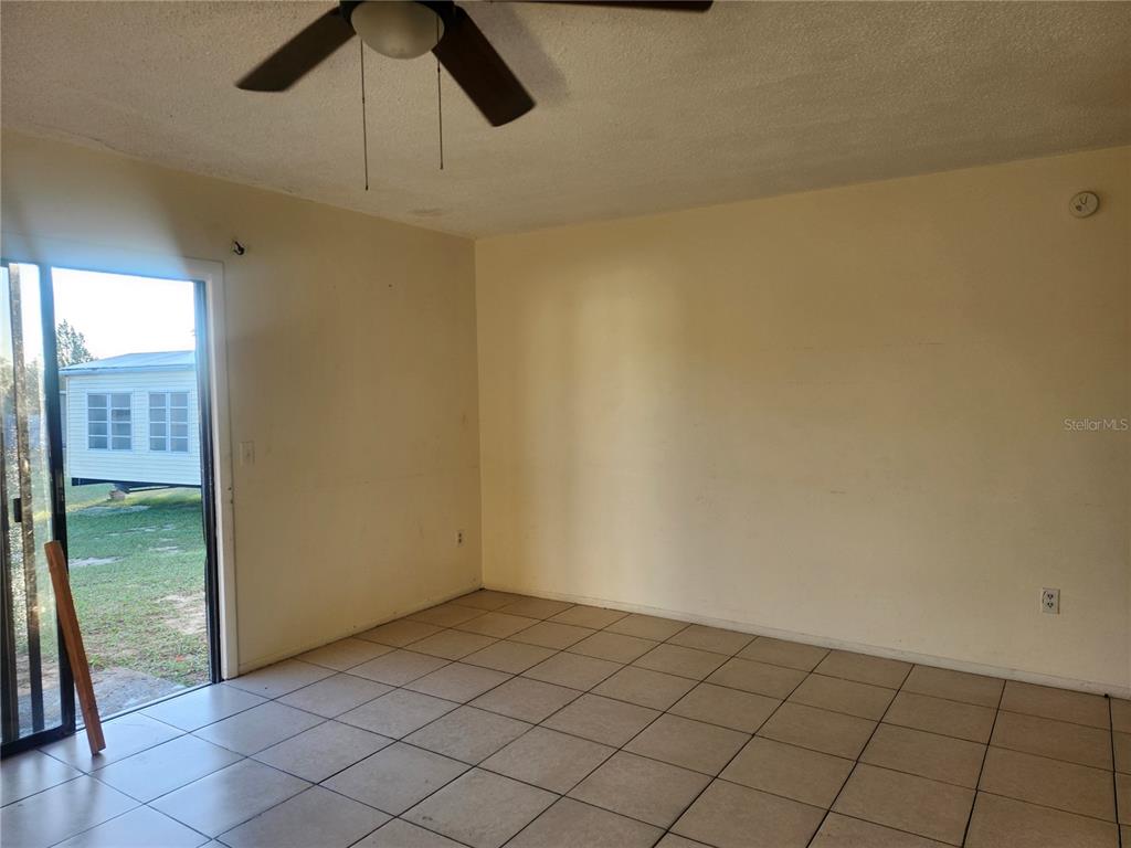 An empty room features beige tile flooring, light-colored walls, a ceiling fan, and sliding doors — 46 PALM ROAD, OCALA, FL