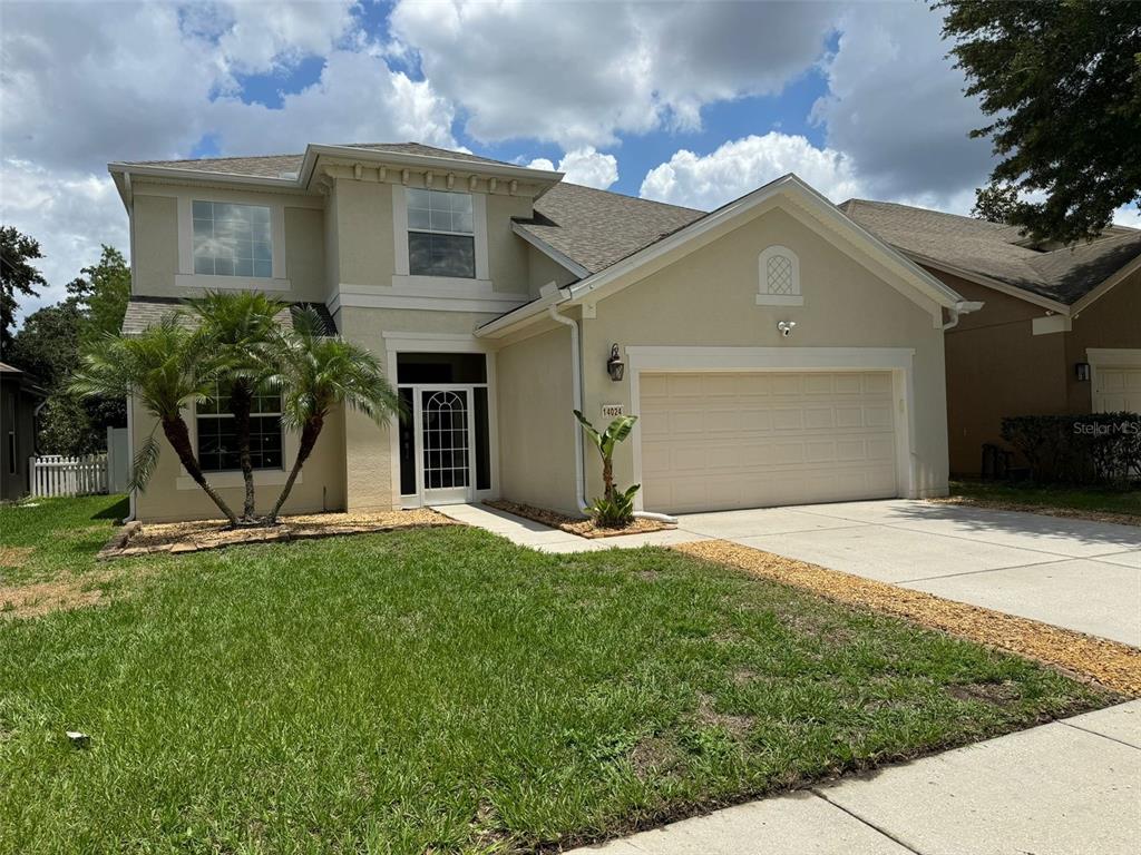 A two-story suburban house features a beige stucco exterior, a two-car garage, and palm trees — 14024 WAKE ROBIN DRIVE, BROOKSVILLE, FL