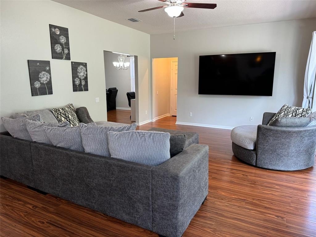 A living room features a gray sectional sofa, a circular chair, and a wall-mounted television — 14024 WAKE ROBIN DRIVE, BROOKSVILLE, FL