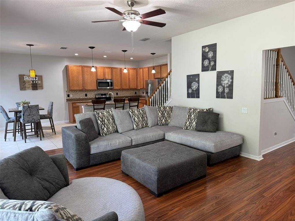 A living room with a gray sectional sofa and ottoman opens to a kitchen area — 14024 WAKE ROBIN DRIVE, BROOKSVILLE, FL