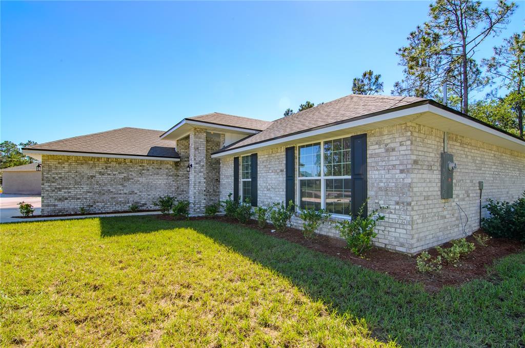 A single-story brick house with a hip roof and dark shutters sits on a lawn — 79 SLUMBER MEADOW TRAIL, PALM COAST, FL