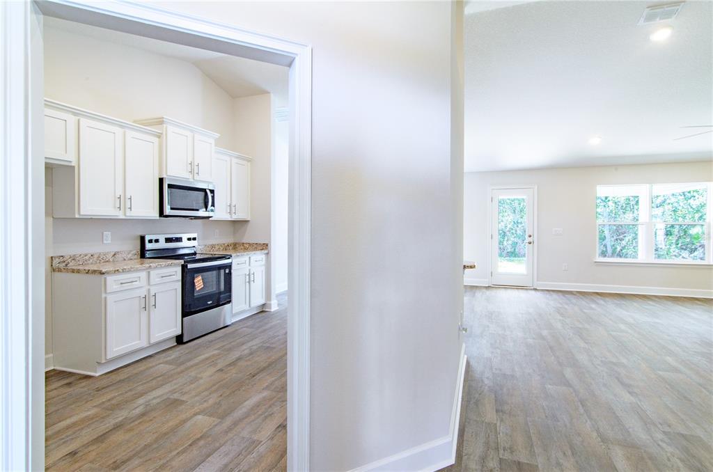 A view through a doorway into a kitchen with white cabinets and wood-look flooring — 79 SLUMBER MEADOW TRAIL, PALM COAST, FL