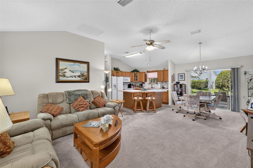 A living room with carpeted floors, a beige sofa, and an open kitchen with wooden cabinets — 1276 NORTHBROOK PLACE, THE VILLAGES, FL