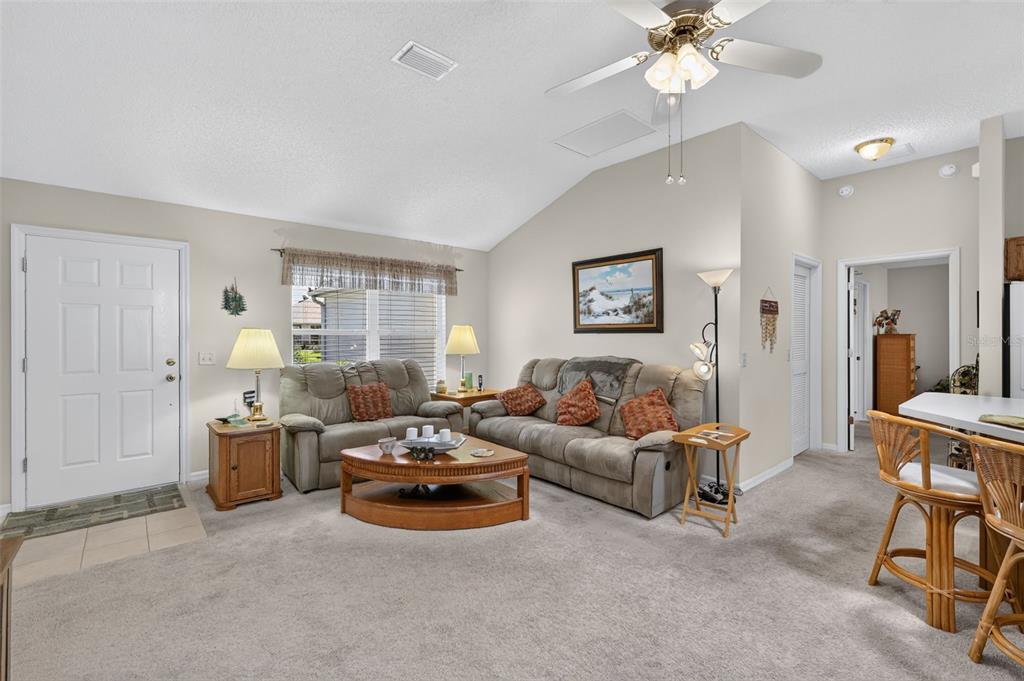 A living room features a vaulted ceiling, two sofas, a coffee table, and carpeted flooring — 1276 NORTHBROOK PLACE, THE VILLAGES, FL