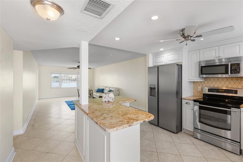 A kitchen with granite countertops and stainless steel appliances opens into a living area — 4775 COVE CIRCLE UNIT 202, ST PETERSBURG, FL
