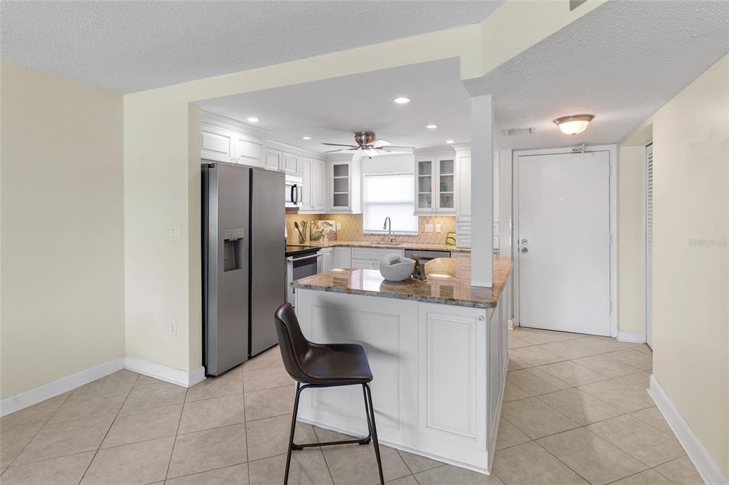 A kitchen with white cabinets, granite countertops, stainless steel appliances, and a breakfast bar island — 4775 COVE CIRCLE UNIT 202, ST PETERSBURG, FL
