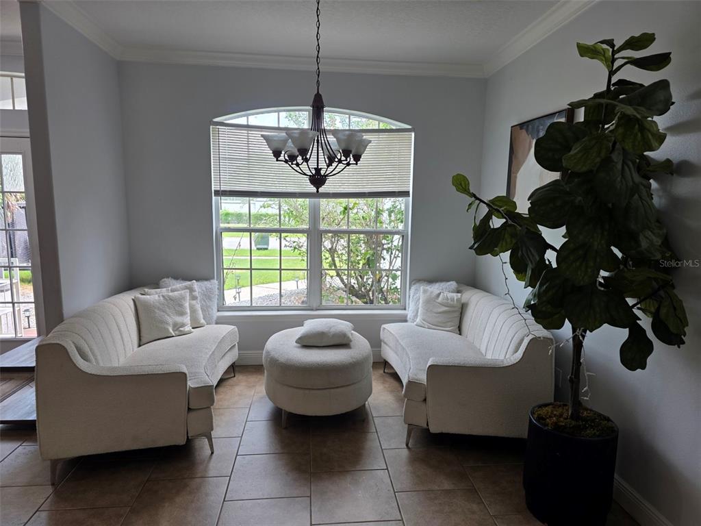 A sunlit sitting area features two cream sofas, a round ottoman, and a large potted plant — 4644 SAWYER ROAD, SARASOTA, FL