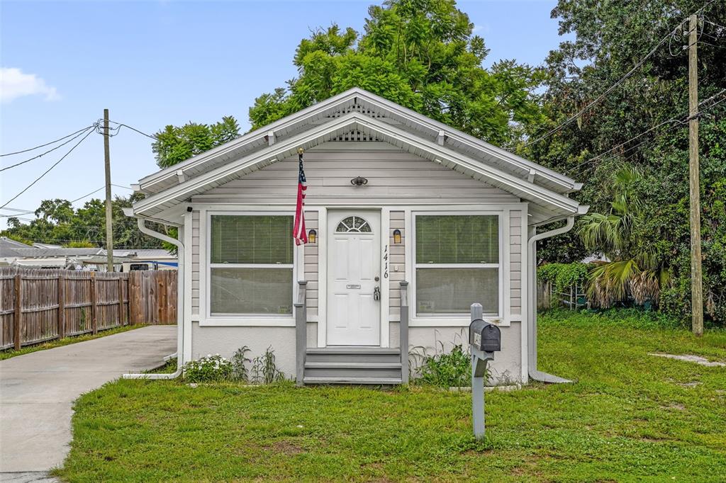 A small, light-gray, single-story house with a front porch, American flag, and concrete driveway — 1416 6TH STREET, ST CLOUD, FL