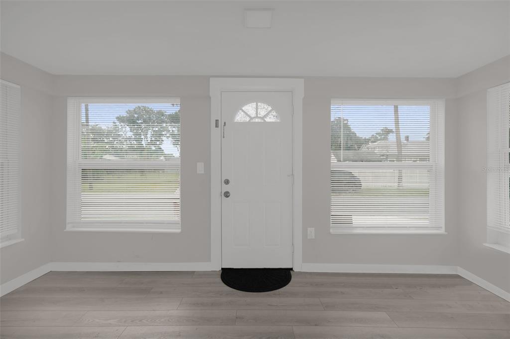 A bright room with light gray walls, wood-look flooring, a white front door, and windows — 1416 6TH STREET, ST CLOUD, FL