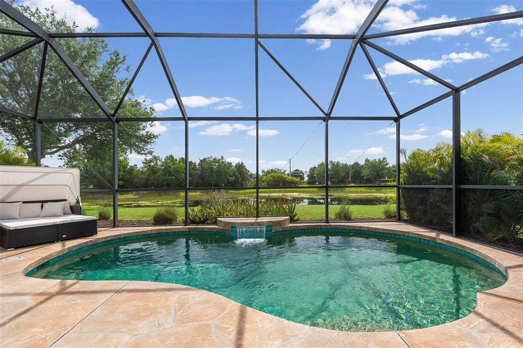A screened-in pool area features a stone deck, a small waterfall, and a lounge chair — 11904 FOREST PARK CIRCLE, BRADENTON, FL