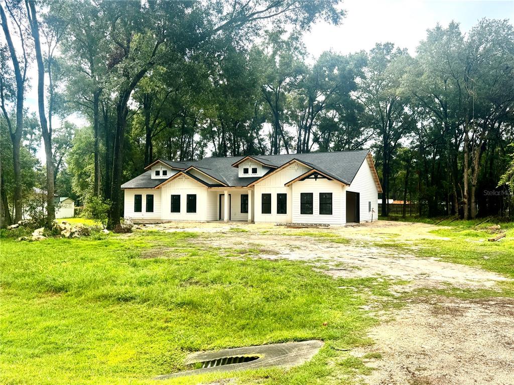 A newly constructed white farmhouse-style home with a dark roof sits on a wooded lot — 23161 NW 183RD LANE, HIGH SPRINGS, FL