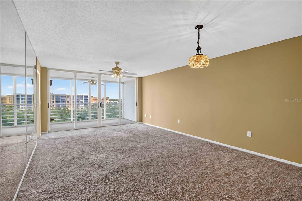 An empty living room features beige walls, brown carpeting, a ceiling fan, and sliding glass doors — 4550 PINEBROOK CIRCLE UNIT 605, BRADENTON, FL