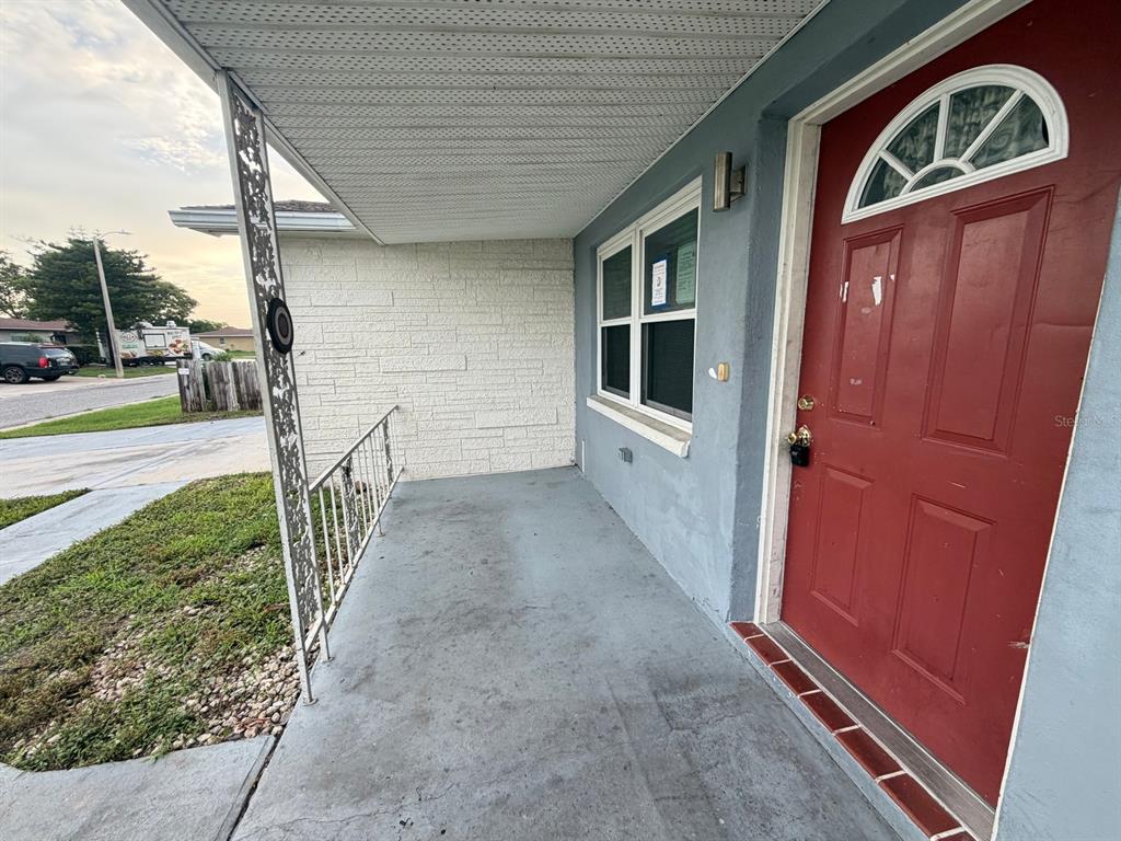 A covered concrete porch features a red front door and a white stone accent wall — 3221 ROXBURY DRIVE, HOLIDAY, FL