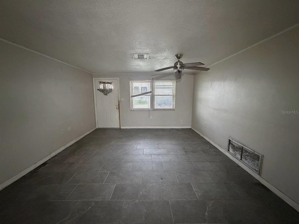 An empty living room features gray tile flooring, a ceiling fan, and a front door — 3221 ROXBURY DRIVE, HOLIDAY, FL