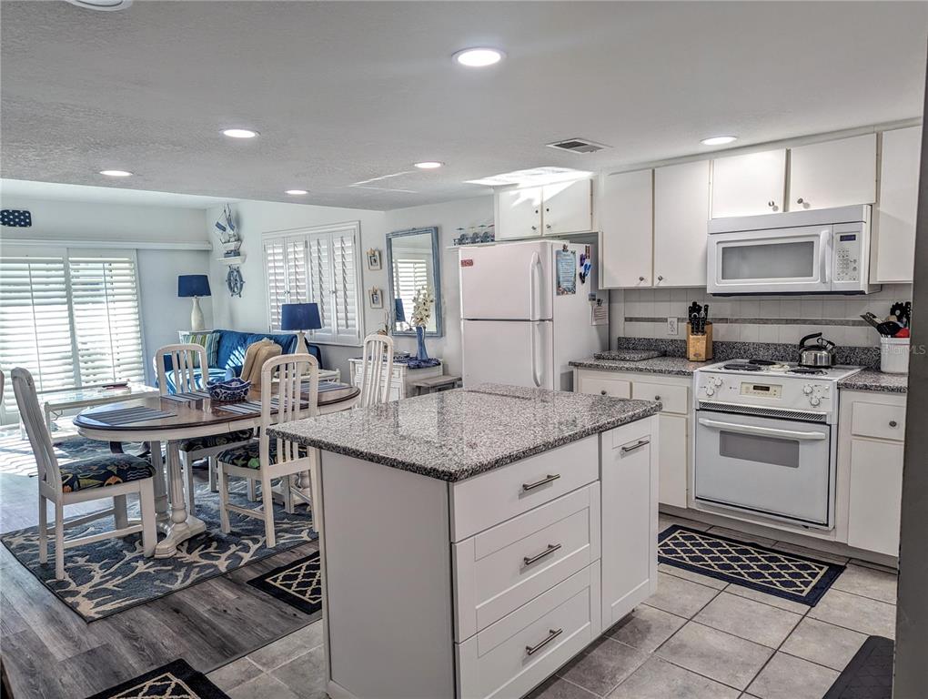 A kitchen with white cabinets, granite countertops, and a central island opens to a dining area — 815 OCEAN SHORE BOULEVARD UNIT 11A, ORMOND BEACH, FL